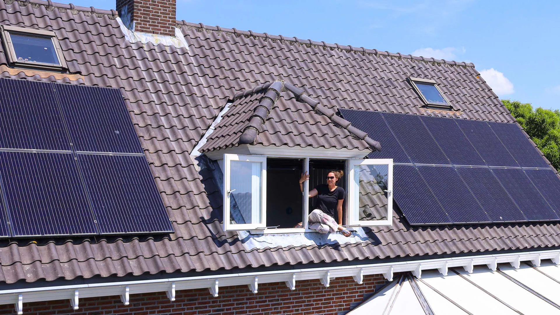 Zonnepanelen op dak woonhuis Zonnepanelen op dak, geplaatst door Greenchoice. Een persoon leunt uit het dakraam.