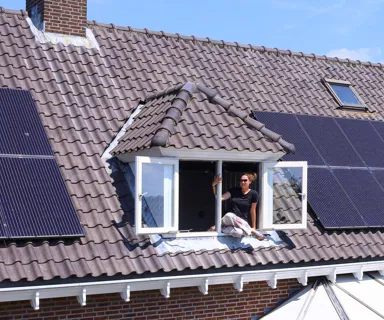 Zonnepanelen op dak woonhuis Zonnepanelen op dak, geplaatst door Greenchoice. Een persoon leunt uit het dakraam.