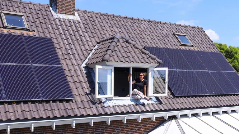 Zonnepanelen op dak woonhuis Zonnepanelen op dak, geplaatst door Greenchoice. Een persoon leunt uit het dakraam.