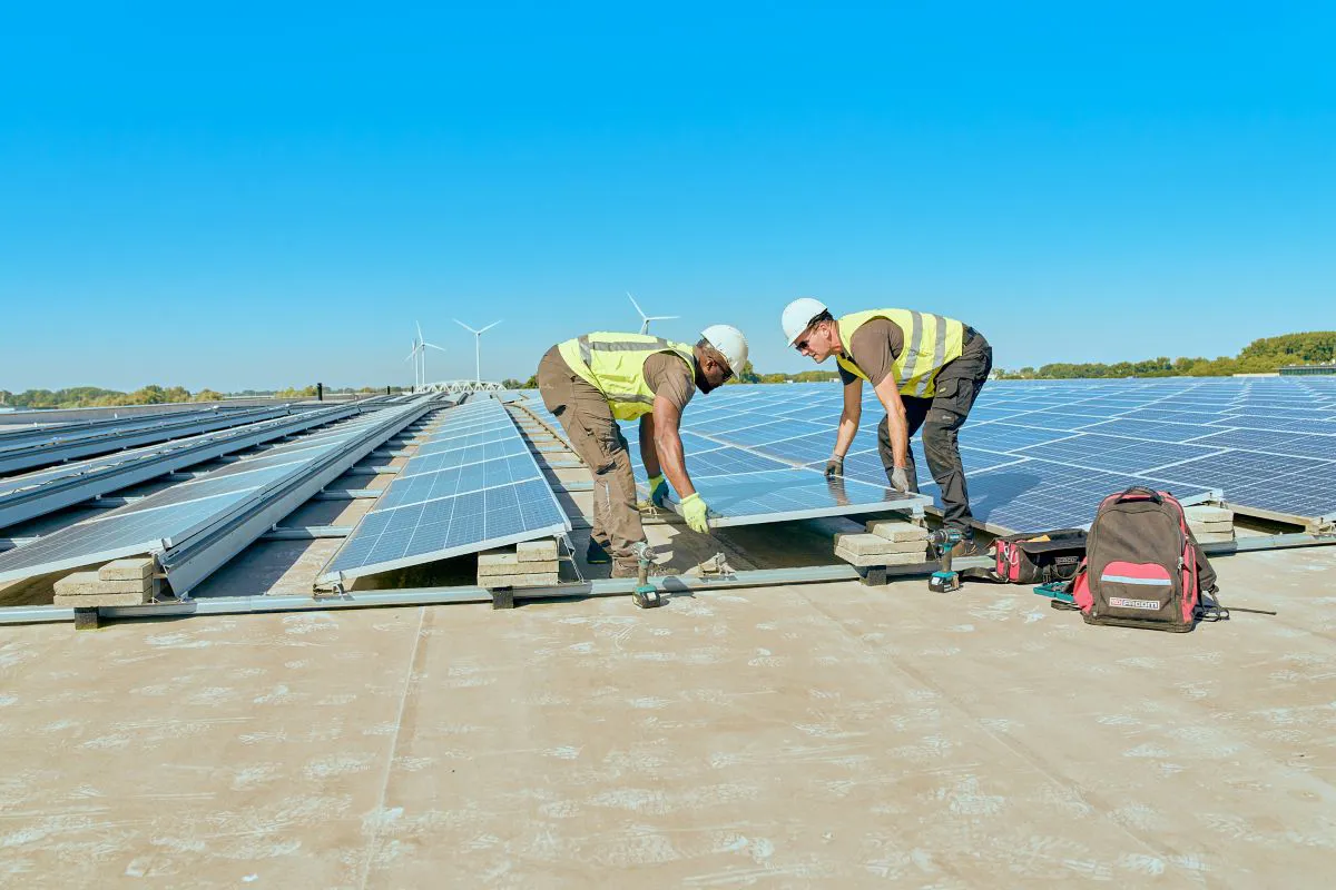 Zonnepanelen op dak plaatsen Twee mannen leggen samen de laatste zonnepaneel neer op een groot plat dak.