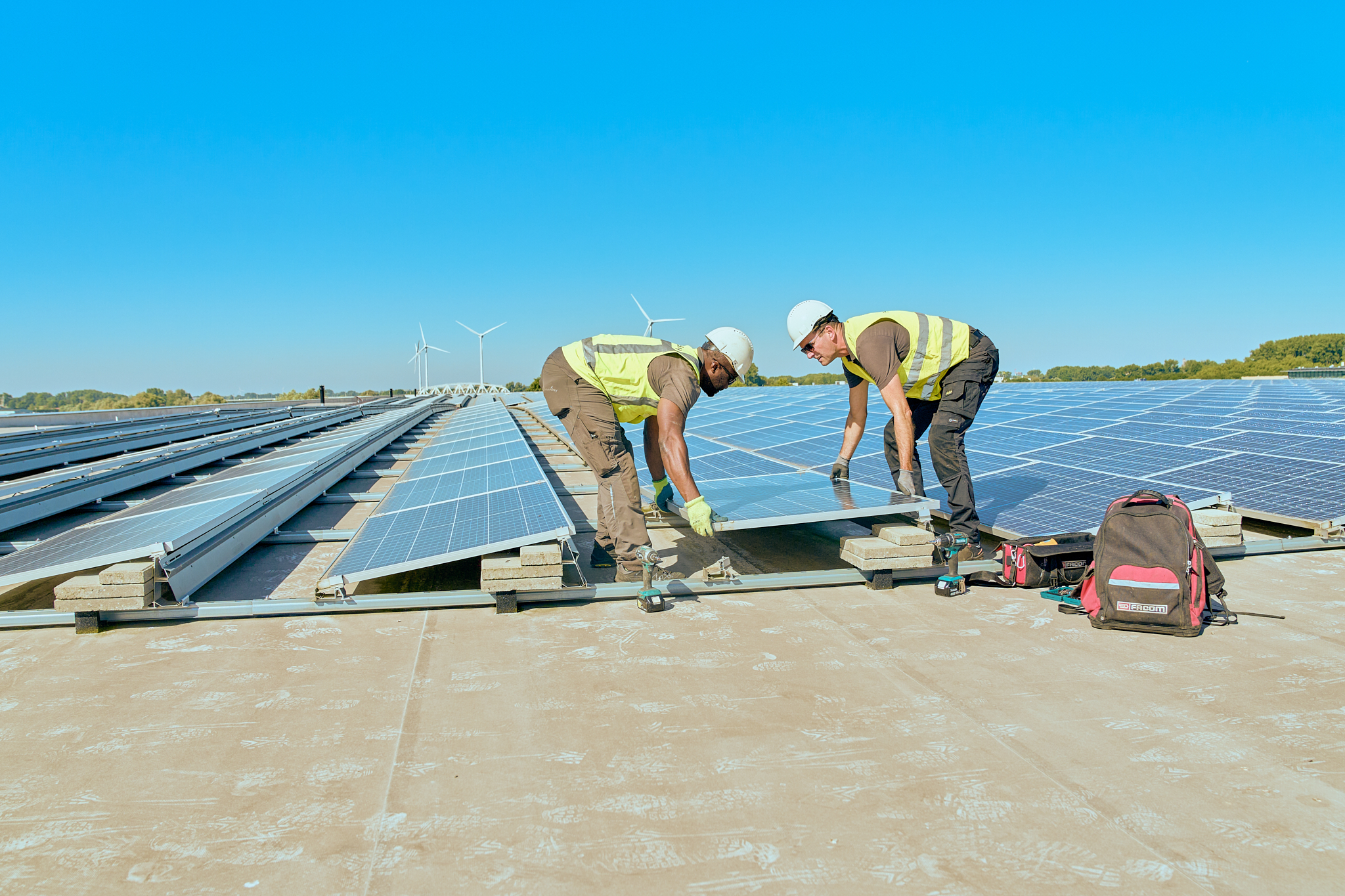 Twee mannen leggen samen de laatste zonnepaneel neer op een groot plat dak. 