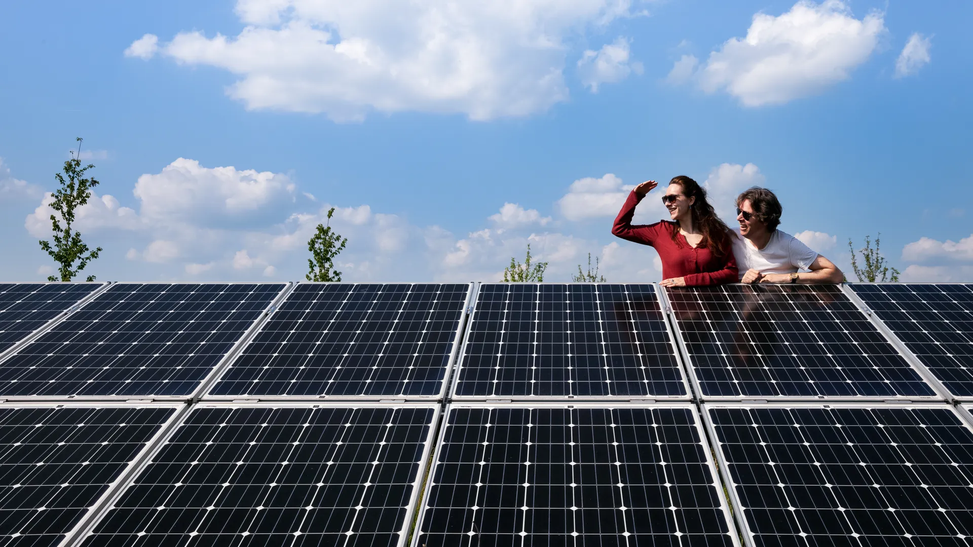 Twee mensen leunen over een rij zonnepanelen en kijken samen naar rechts.