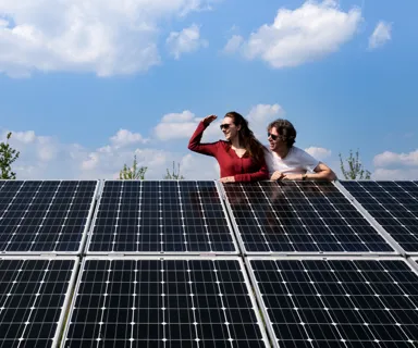 Man en vrouw in zonnepanelenpark Twee mensen leunen over een rij zonnepanelen en kijken samen naar rechts.