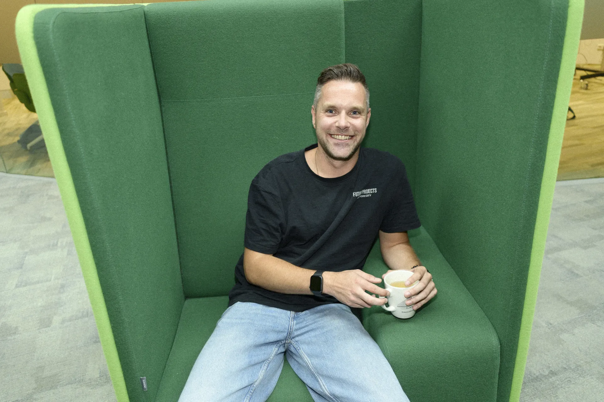 Rowin Visscher Een man zit ontspannen in een comfortabele stoel, met een rustige en tevreden uitstraling. Hij leunt iets achterover met een kop koffie in zijn handen.