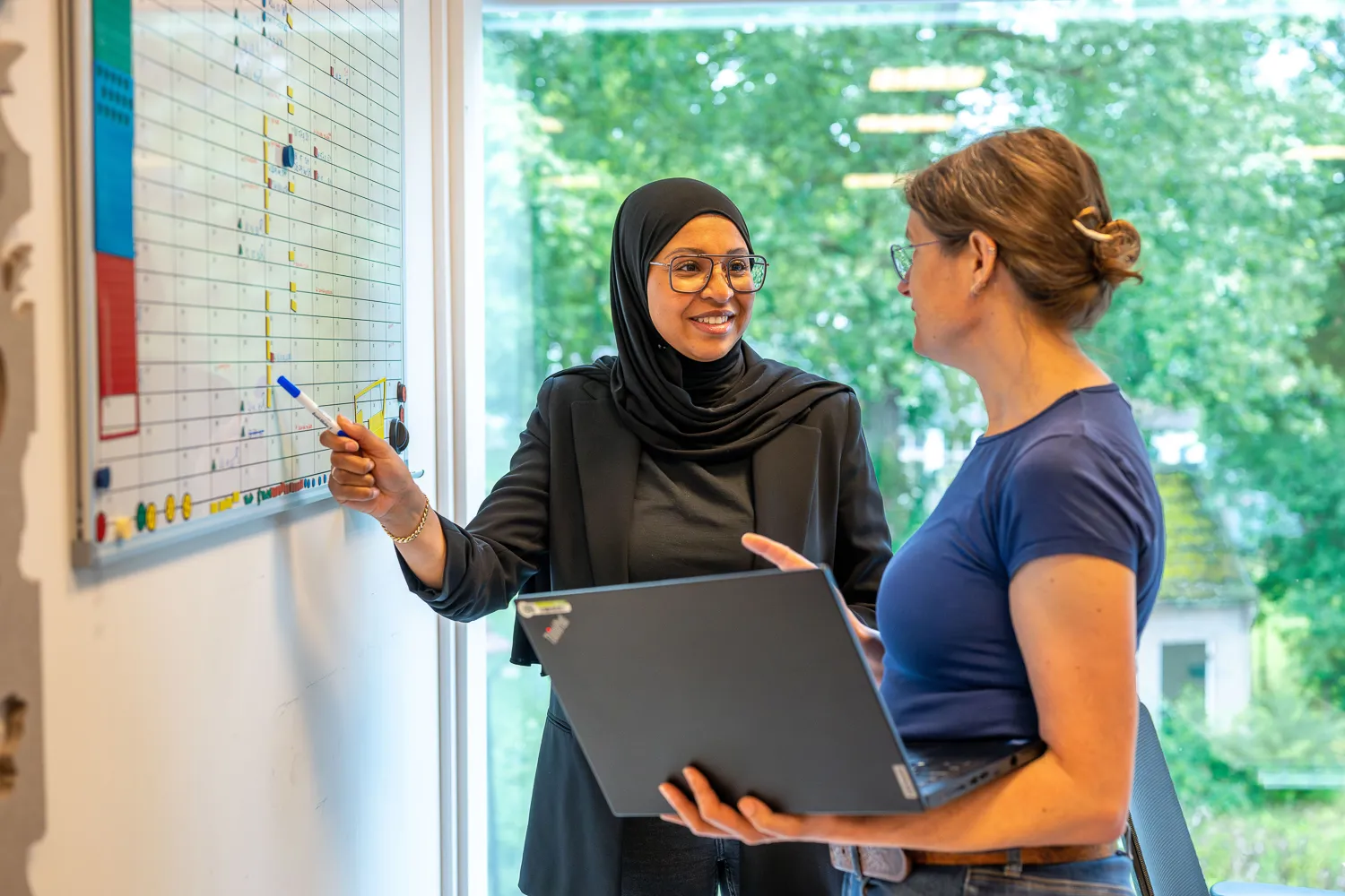 Twee collega's in gesprek tijdens een stand-up meeting bij een whiteboard