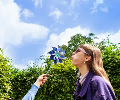 Vrouw en windmolen Vrouw blaast tegen een papieren windmolentje. Ze is opgewekt, net als de windstroom van Greenchoice.