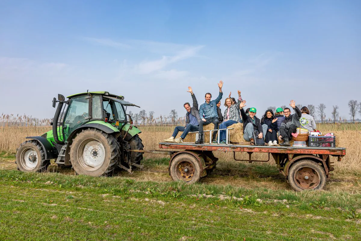 Tractor in het groen Collega's zwaaien vrolijk naar de camera terwijl ze op een aanhanger achter een tractor zit, omringd door groene natuur.
