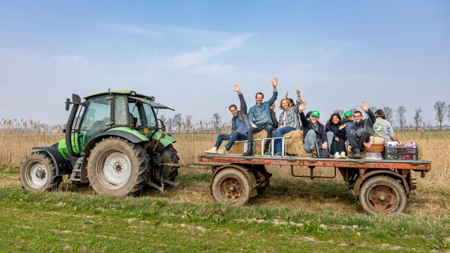 Tractor in het groen Collega's zwaaien vrolijk naar de camera terwijl ze op een aanhanger achter een tractor zit, omringd door groene natuur.