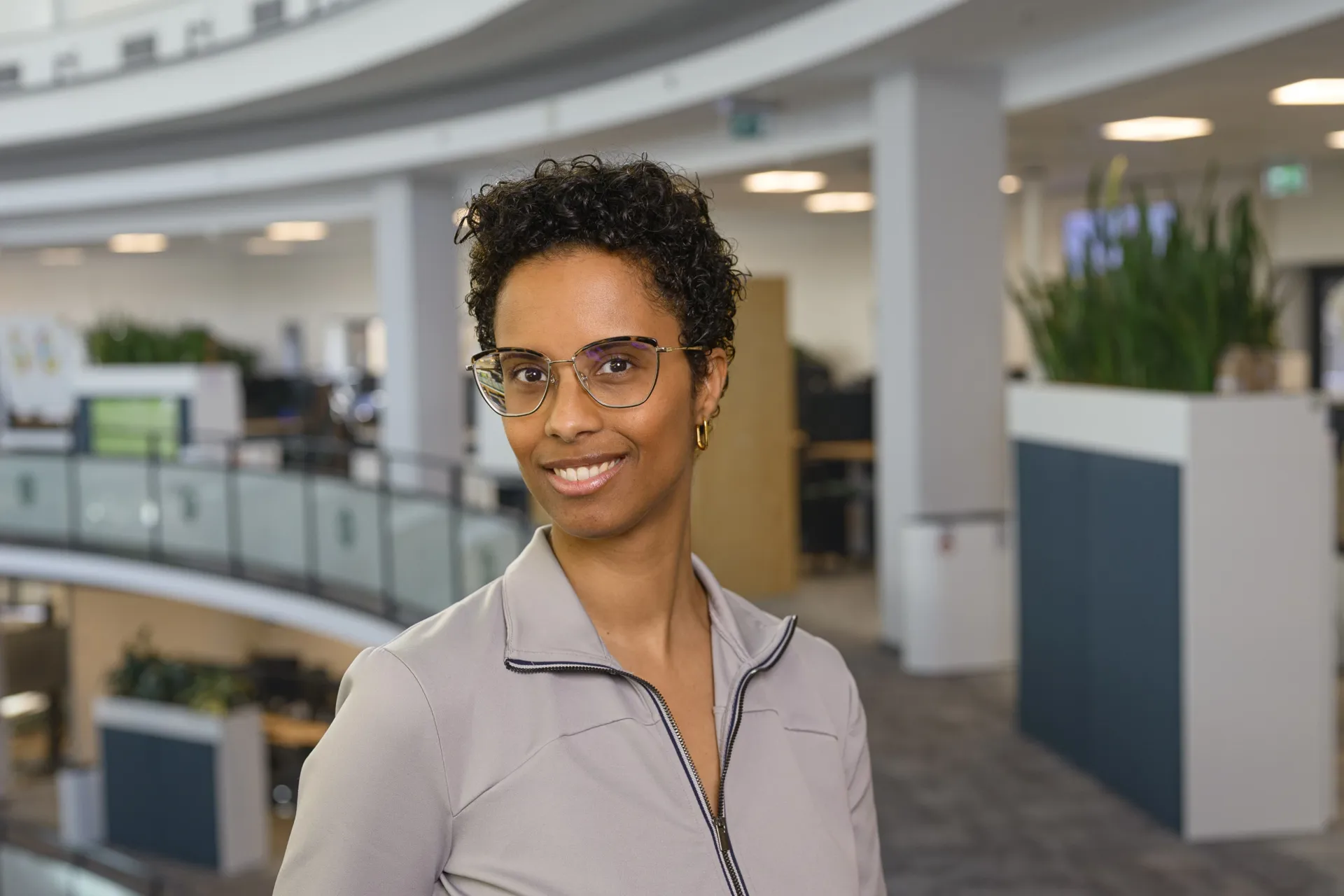 Liliana dos Santos Een portret foto van Liliana. Ze lacht in de camera. Op de achtergrond zie je de tweede verdieping van het kantoor.