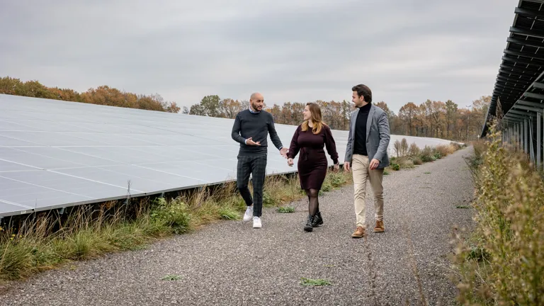Greenchoice Integrated Drie collega's lopen buiten over een veld vol zonnepanelen. De twee mannen en een vrouw zijn druk in gesprek.
