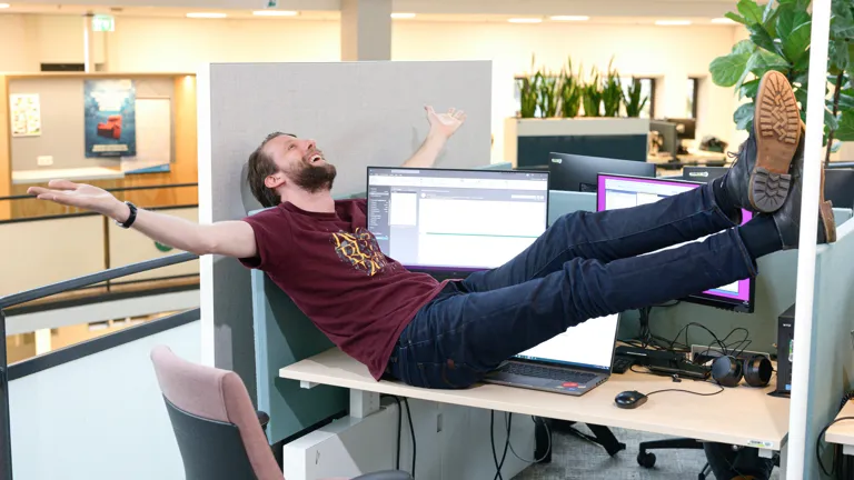 Collega neemt een creatieve koffiepauze: hij ligt languit op het bureau, zichtbaar tevreden