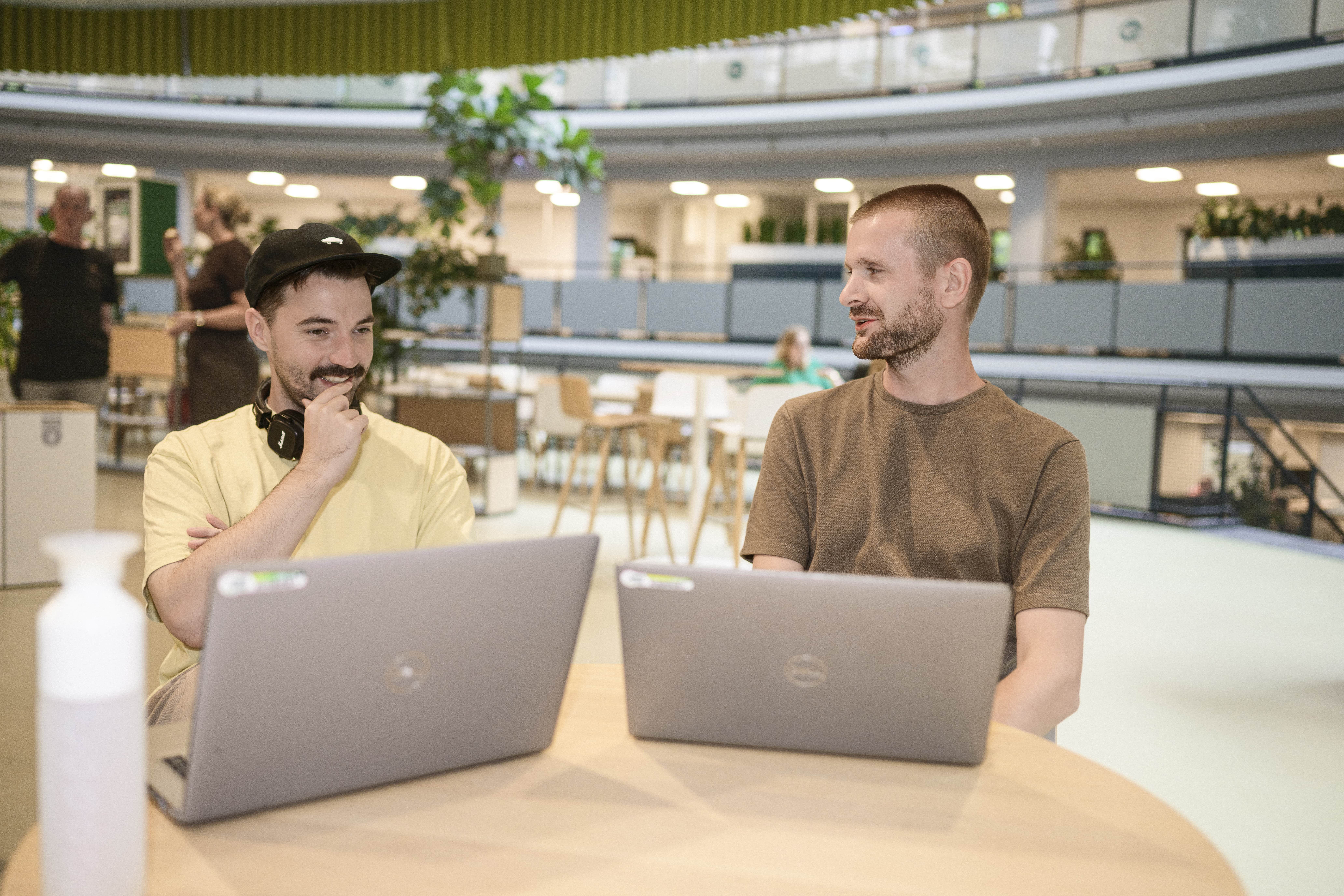 Twee collega's hebben een informeel overleg met de laptop in het Groene Hart (onze lunchruimte). Ze ogen ontspannen en kijken naar elkaar of het scherm. 
