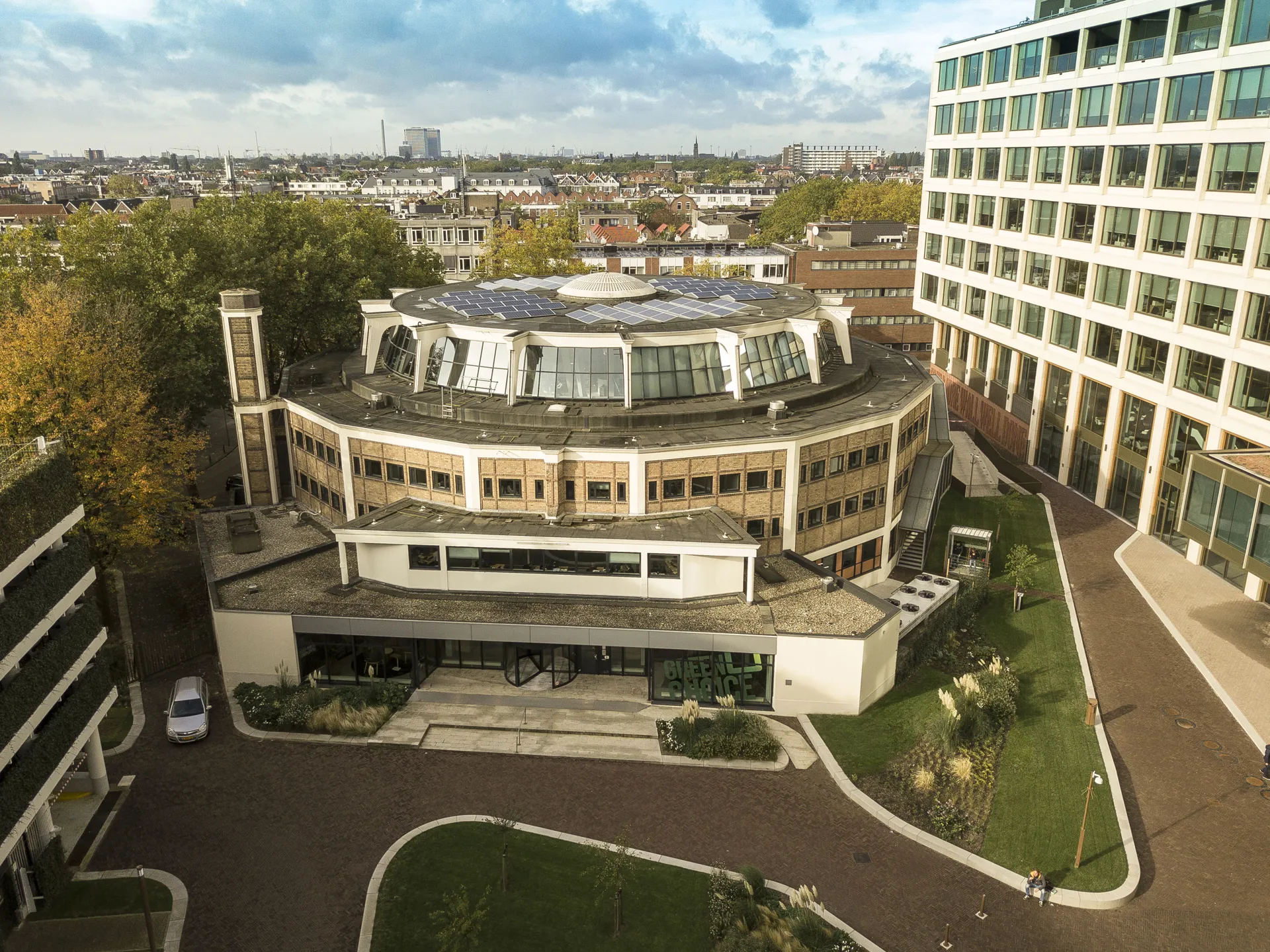 Historisch kantoorpand omgeven door groen, gelegen tussen moderne hoogbouw, met de stad Rotterdam op de achtergrond.
