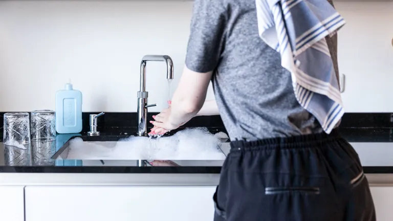 Handen wassen waterverbruik Een persoon wast hun handen in de keuken.