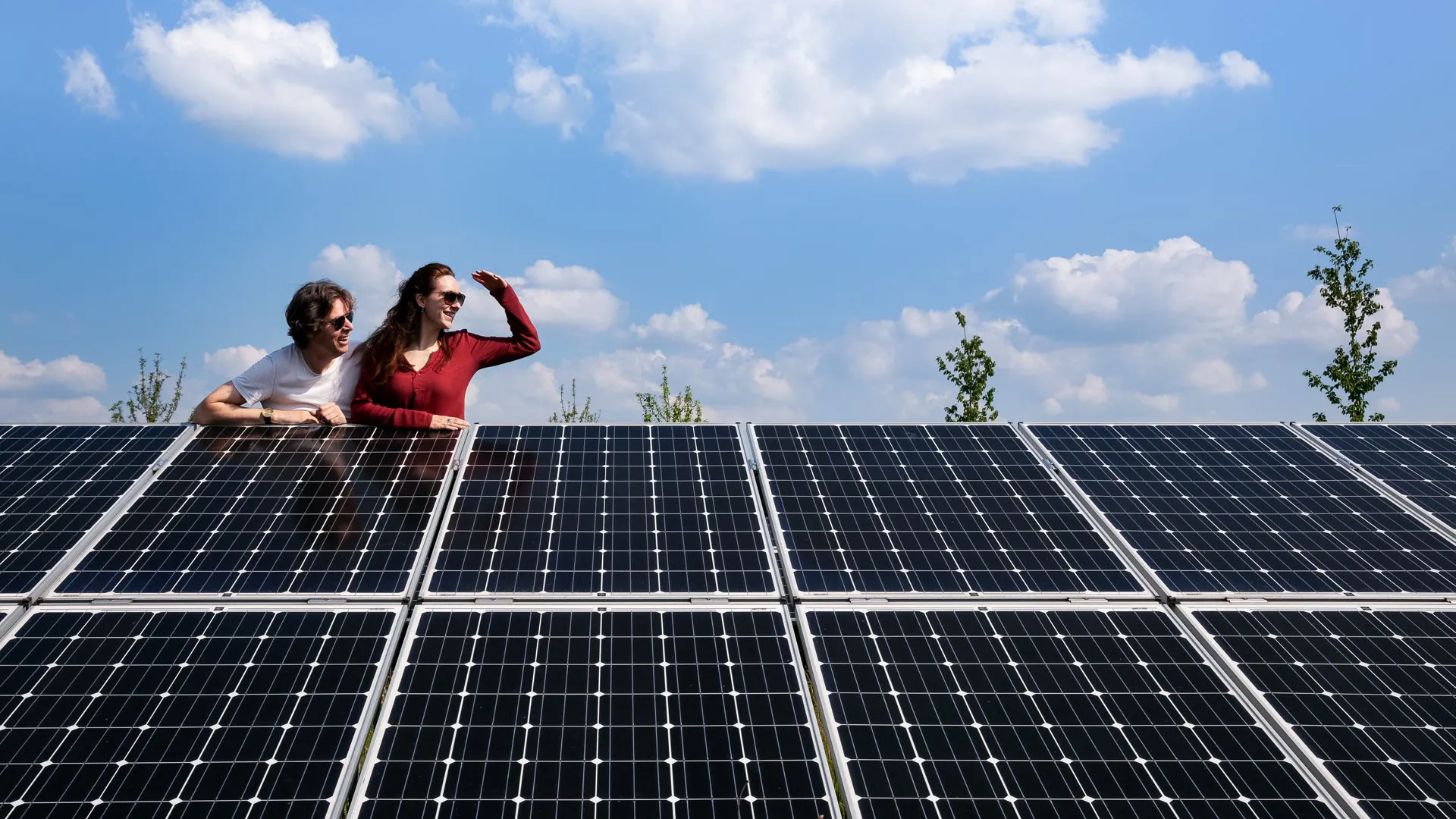 Man en vrouw in zonnepanelenpark Twee mensen leunen over een rij zonnepanelen en kijken samen naar rechts. Met zonnepanelen maak je een stap naar de toekomst.