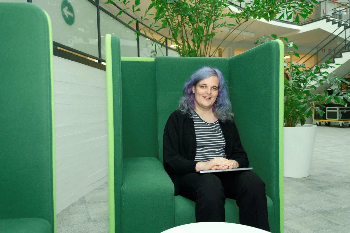June Don Een collega zit ontspannen in een moderne ontspanningsruimte met comfortabele zitmeubels. Om de collega heen zie je een minimalistisch interieur en planten op de achtergrond.