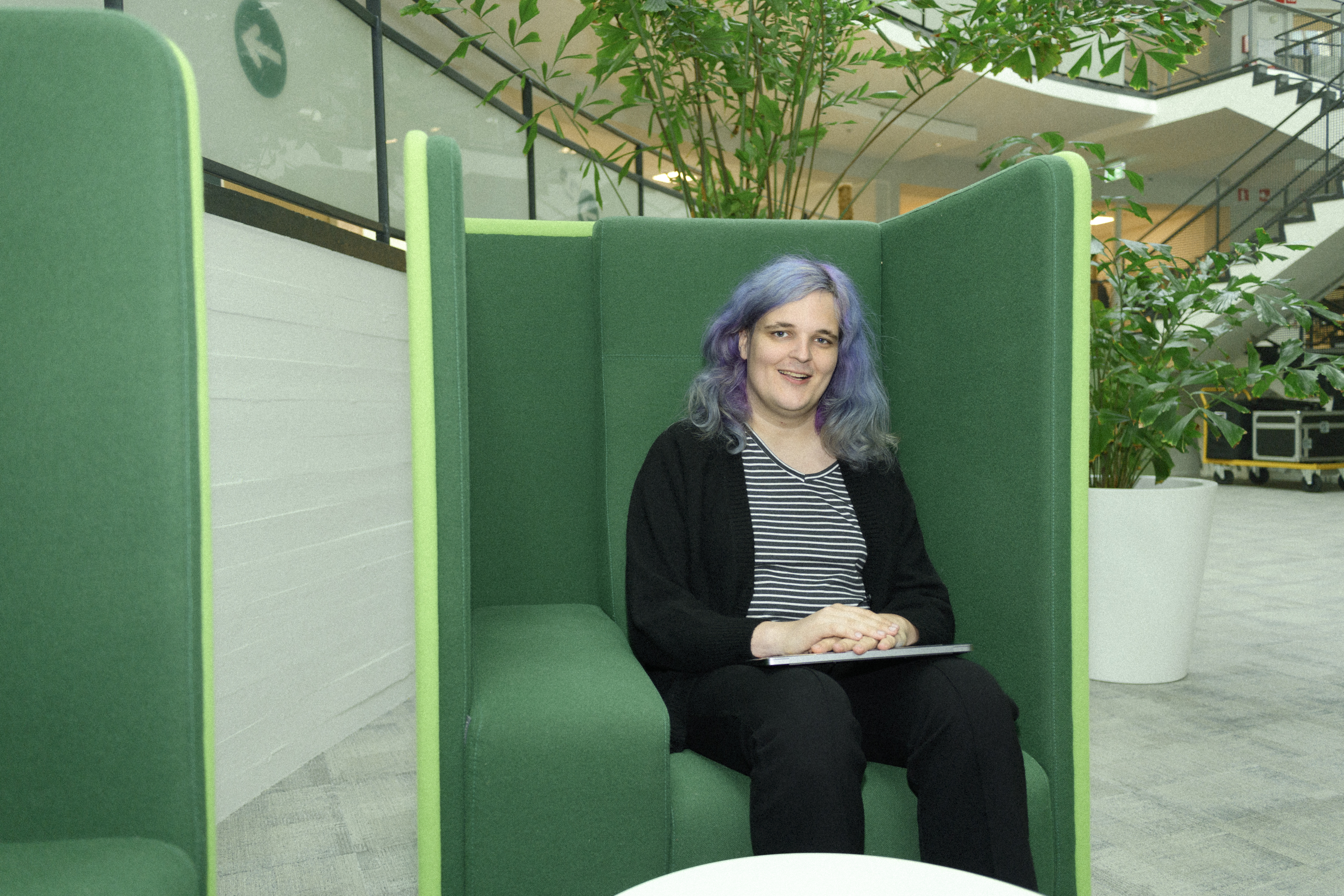 Een collega zit ontspannen in een moderne ontspanningsruimte met comfortabele zitmeubels. Om de collega heen zie je een minimalistisch interieur en planten op de achtergrond.